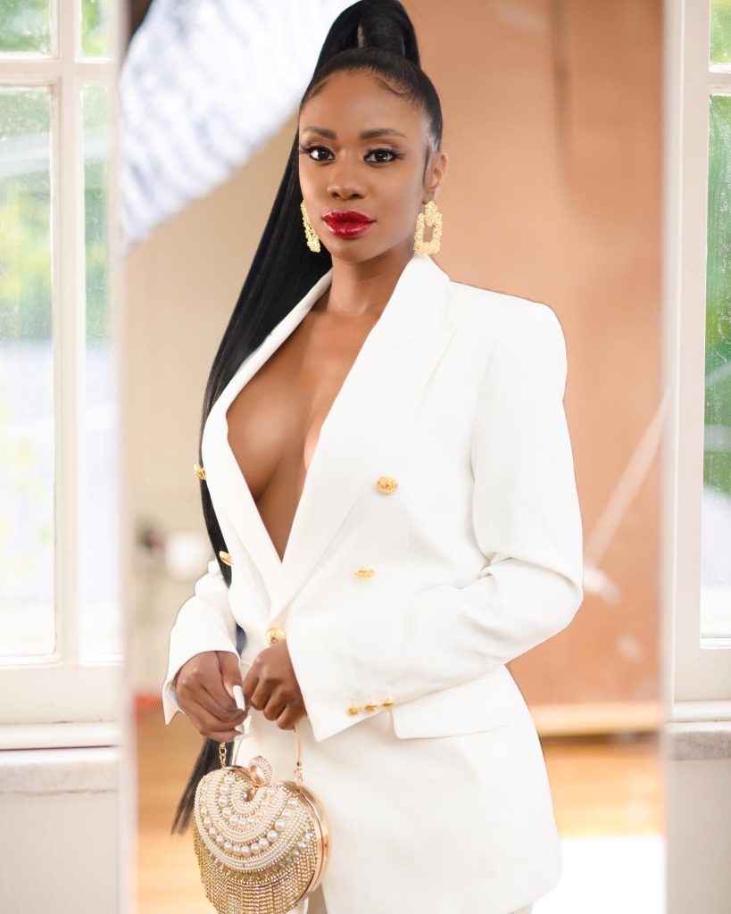 Sucoyia posing in a white blazer dress with gold accessories and a pearl handbag.